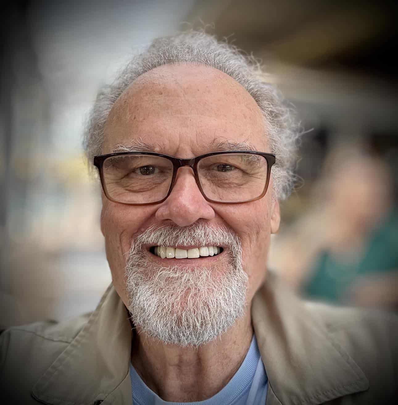 Michael Gravette smiling with glasses and white beard in an outdoor setting.