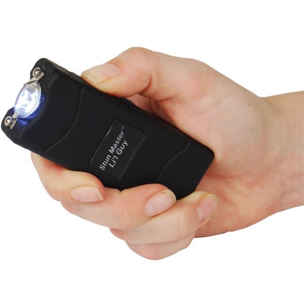 Hand holding a compact black stun device with a bright LED light activated.