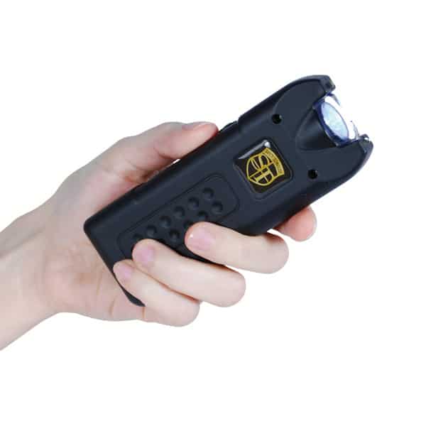 Hand holding a black stun gun for self-defense, with safety switch and ergonomic grip.