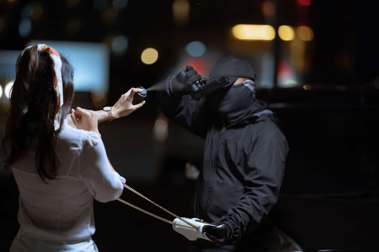 Woman using pepper spray for self-defense against masked attacker at night.